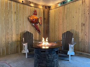 Une pièce chaleureuse avec un foyer en pierre, deux fauteuils Adirondack, des murs en bois et une grande décoration représentant un poisson.