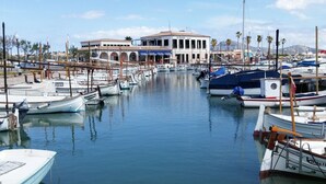 Un puerto deportivo con varias embarcaciones amarradas, un edificio con arcos y un cielo despejado.