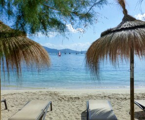 A beach with two thatched umbrellas, a sandy shore, and a calm sea with sailboats. - Apartamento La Llimona - Nice apartment near the beach in Port de Pollença (Port de Pollença)