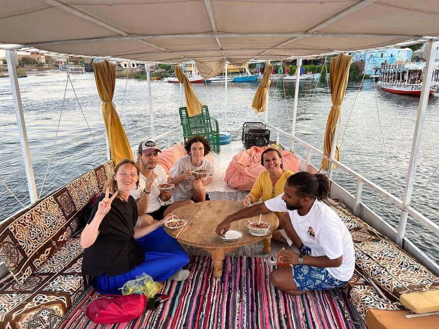 Un grupo de personas cenando en un barco con vistas al agua y a otros barcos al fondo.