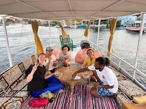 A group of people dining on a boat with a view of the water and other boats in the background. - Nubian Kindom Aragheed House (Aswan)