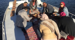 A group of people seated on a boat with a table set for a meal. - Nubian Kindom Aragheed House (Aswan)