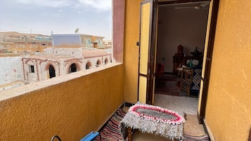 A balcony with a view of buildings, a patterned rug, and a small table with a chair.