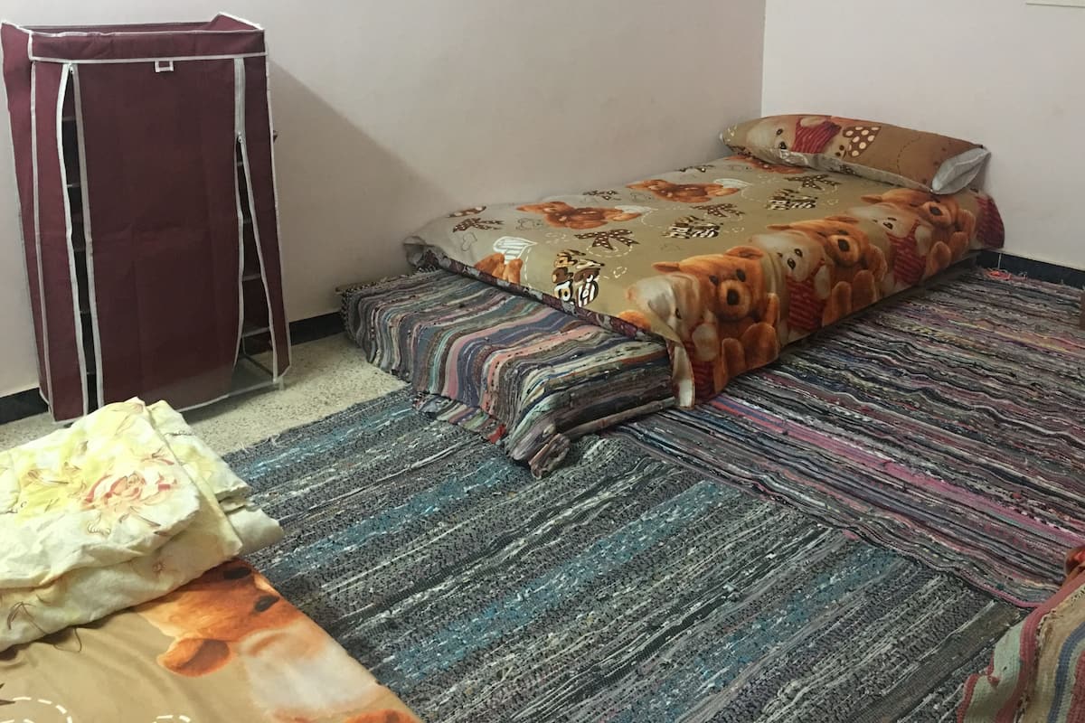 A bedroom with a bed, a striped rug, a wooden wardrobe, and a small table with a water bottle.