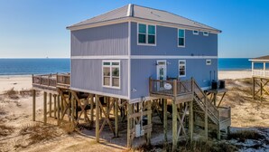 A two-story beach house with a wooden deck and stairs, located on a sandy beach with the ocean in the background. - Gulf Front, Private Heated Pool, Pet Friendly, 2 Master Suites! – Island Time IV (Dauphin Island)