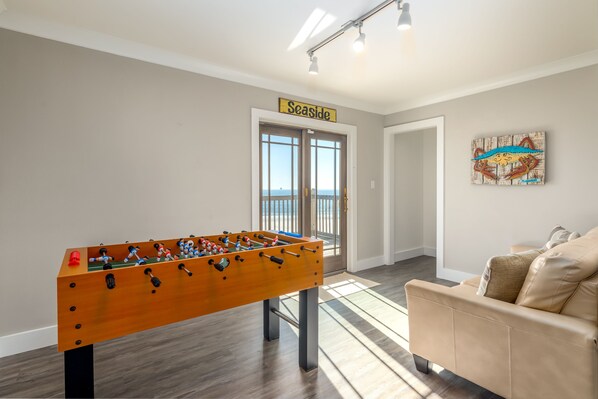 A room with a foosball table, a sofa, a door labeled "Seaside," and a painting on the wall.