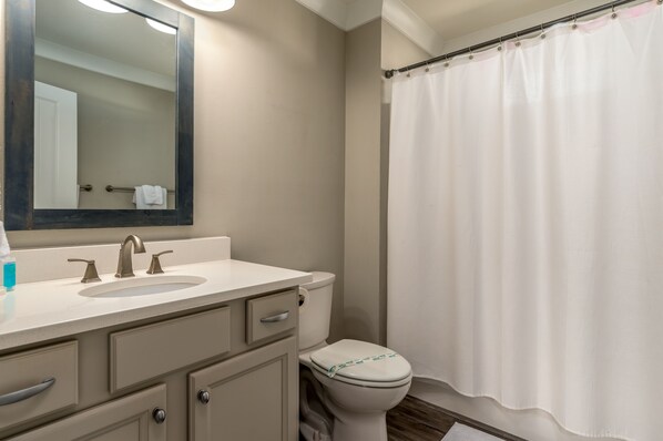 A bathroom with a sink, mirror, toilet, and shower curtain.