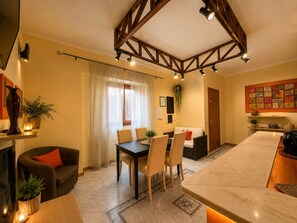 Un salon chaleureux avec une cheminée, un coin repas avec une table et des chaises, et une cuisine dotée d’un grand îlot central.