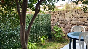 A stone wall, a tree, and a plastic chair in a garden area. - Andrea Apartment.  (Portoscuso)