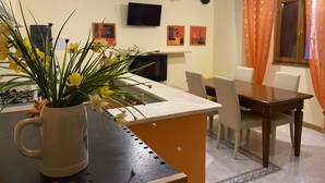 Un coin repas avec une table et des chaises, un téléviseur fixé au mur et un vase de fleurs posé sur une table.