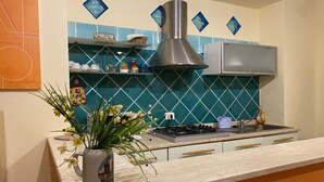 Une cuisine équipée d’une cuisinière à gaz, d’une hotte en acier inoxydable, d’un crédence de couleur turquoise et d’un vase rempli de fleurs posé sur le plan de travail.