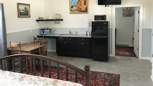 Eine kompakte Küche mit Mikrowelle, Toaster und Kühlschrank. Ein Esstisch mit Stühlen und ein kleiner Teppich sind vorhanden.