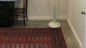 Ein Zimmer mit einem Holzstuhl, einer weißen Stehlampe, einem Bild von Herbstlaub und einem roten Teppich mit Muster.