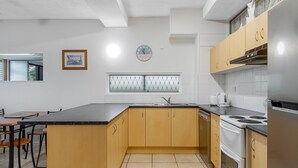 Eine moderne Küche mit Holdekor-Schränken, einer schwarzen Arbeitsplatte, einem Edelstahlherd und einem Fenster mit Jalousien.