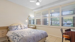 Ein Schlafzimmer mit einem Bett, einem Nachttisch, einem Sessel und einem Fenster mit Jalousien.