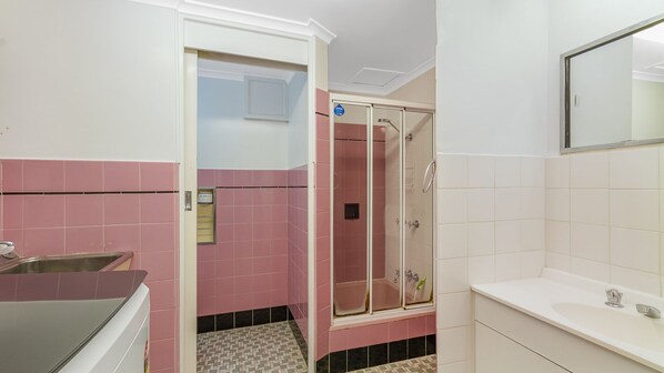 A bathroom with pink and white tiles, a glass shower enclosure, a sink, and a mirror. - Blue Pacific 1 Beachside neat and tidy unit in Tugun (Tugun)
