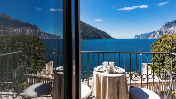Un balcón con una mesa lista para dos personas, con vistas a un cuerpo de agua y montañas.