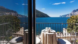 A balcony with a table set for two, overlooking a body of water and mountains.