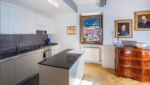 Una cocina moderna con armarios blancos, encimera negra y horno integrado. Se observa una ventana con vistas a edificios y árboles.
