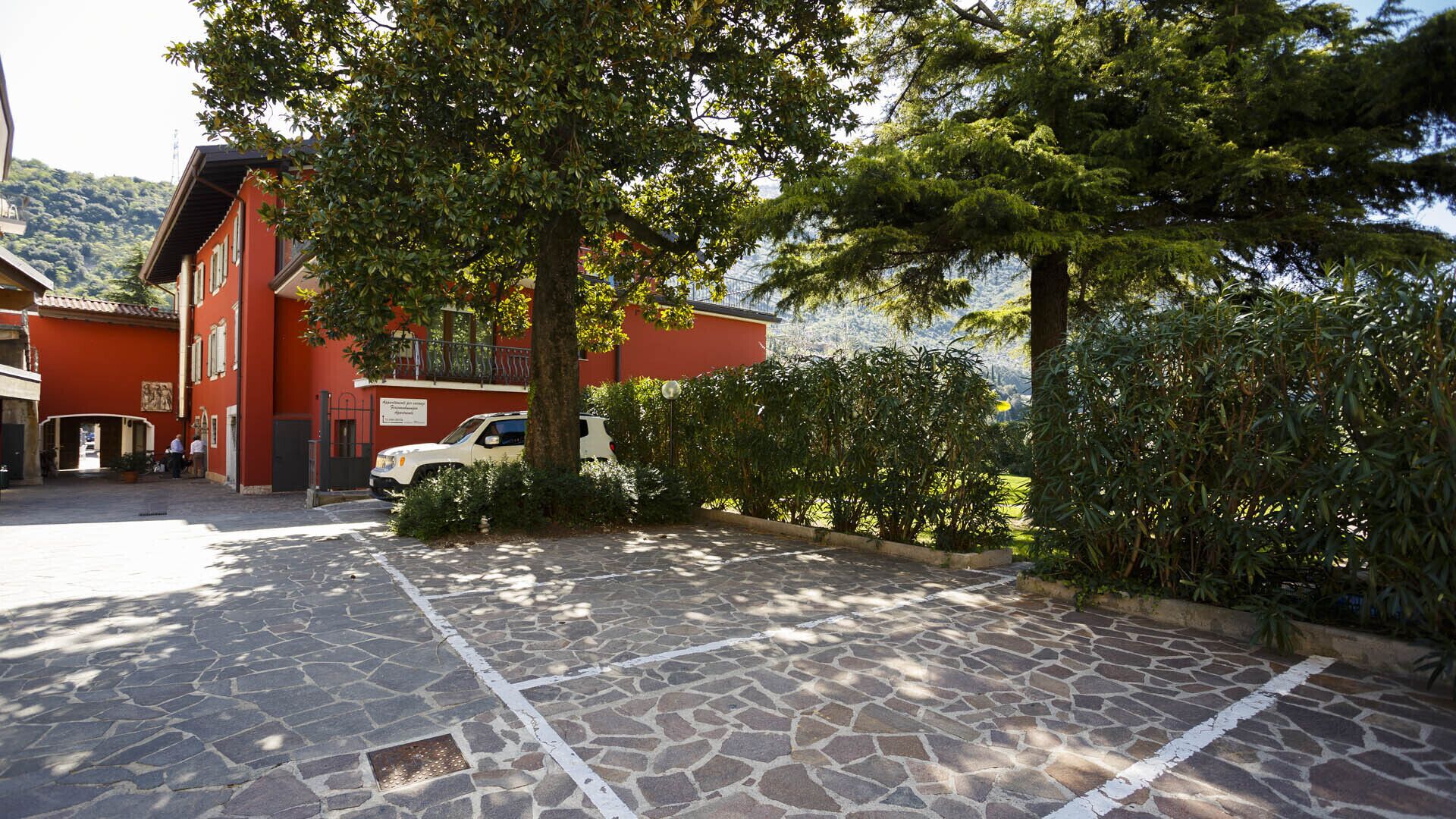 A stone-paved parking area with a white car parked in front of a red building with a balcony.