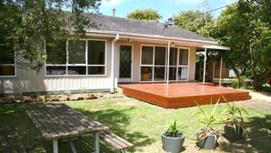 Una casa con un patio in legno, un tavolo da esterno e piante in vaso.