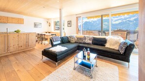 A modern living room with a sectional sofa, a coffee table, and a view of mountains through large windows. - Chalet Am Acher - Luxury and Chic (Wengen)
