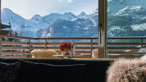 A balcony with a wooden railing, a table with a vase of flowers, and a bottle of champagne. - Chalet Am Acher - Luxury and Chic (Wengen)