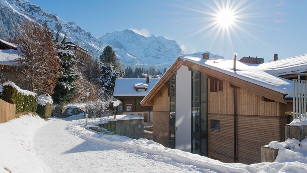 A wooden chalet with a glass facade, surrounded by snow-covered mountains and a clear sky. - Chalet Am Acher - Luxury and Chic (Wengen)