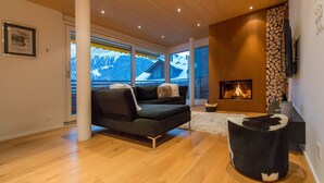 A modern living room with a fireplace, a sofa, and a view of a snowy mountain. - Chalet Am Acher - Luxury and Chic (Wengen)