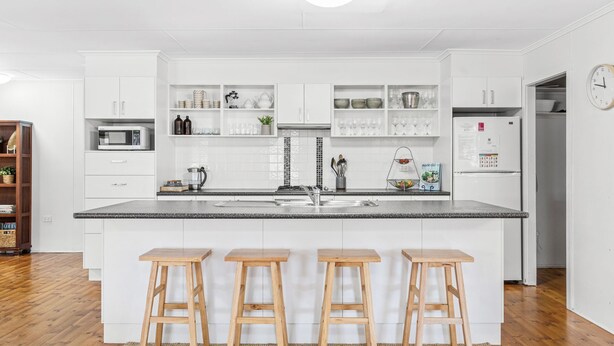 Een moderne keuken met witte kastjes, een granieten aanrecht en drie houten krukken.