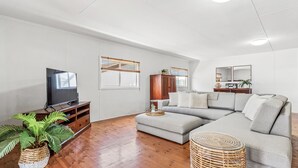 Een moderne woonkamer met een hoekbank, een flatscreen televisie, houten vloeren en een groot raam met uitzicht.