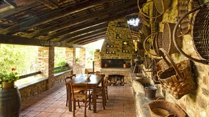 Ein rustikaler Essbereich im Freien mit Kamin aus Stein, Holzmöbeln und Körben an der Wand.
