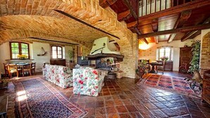 Ein geräumiger Raum mit Steindecke, Holzbalken, Kamin und Essbereich mit Tisch und Stühlen.