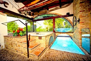 A stone pool with a glass enclosure, a wooden deck, and a view of greenery outside. - Exclusive villa with 8 x 18 swimming pool, sauna, whirlpool and billiards.   (San Luigi)