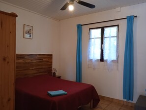 Une chambre à coucher avec une tête de lit en bois, une couvre-lit rouge, une serviette bleue, une table de chevet avec une lampe et une fenêtre avec des rideaux bleus.