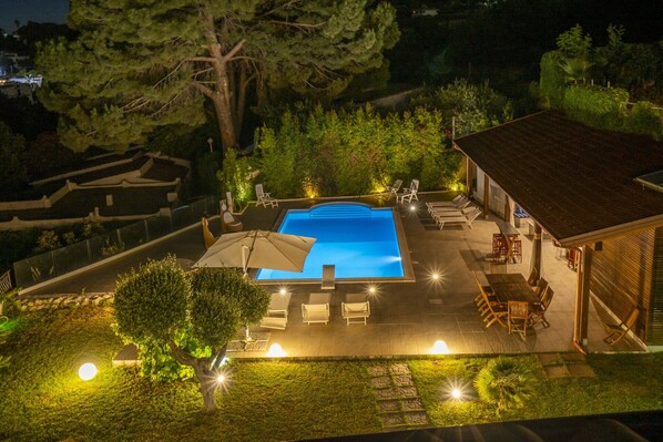 A swimming pool with lounge chairs and a covered seating area, surrounded by trees and a well-lit patio. - Villa Anna, for 10/13 people, with private pool and near the beach (Ricadi - Capo Vaticano)