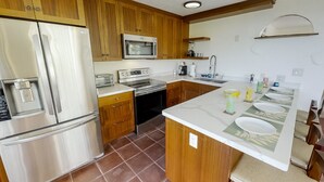 Eine Küche mit Holzschränken, einem Edelstahlkühlschrank, einer Mikrowelle, einem Backofen, einer Spüle und einer Arbeitsplatte mit Spüle und Geschirrgestell.