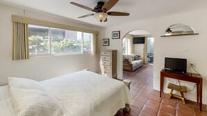 Ein Schlafzimmer mit Bett, Schreibtisch inklusive Computer, Deckenventilator und Blick ins Freie.