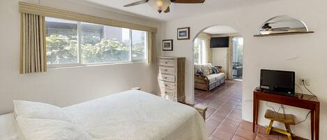 A bedroom with a bed, a desk with a computer, a ceiling fan, and a view of the outside.