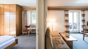 A hotel room with a bed, a sofa, a table with a bowl of fruit, a chair, a desk, and a lamp.