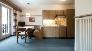 A compact kitchen with wooden cabinets, a dining area with a table and chairs, and a television on a stand.