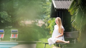 A person sitting on a bench by a poolside with a wicker basket beside them.
