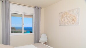 Een slaapkamer met een bed, een stoel, een raam met gordijnen en een wand met een bloemschilderij.