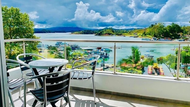 En balkon med et bord og stole, der kigger ud over en lysthavn med både og grønt.
