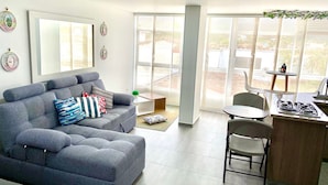 En moderne stue med en grå sofa, et lille sofabord og et spiseområde med bord og stole.