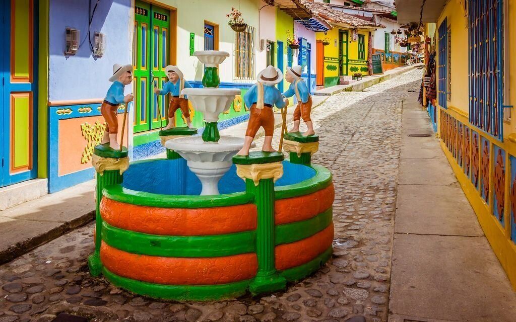 A colorful street scene with a central fountain and statues.