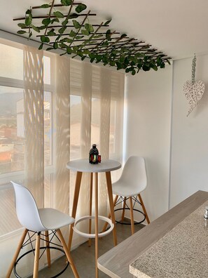 Una habitación moderna con una mesa redonda y dos sillas blancas, una planta colgante y una decoración con forma de corazón en la pared.