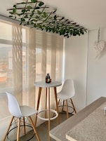Una habitación moderna con una mesa redonda y dos sillas blancas, una planta colgante y una decoración con forma de corazón en la pared.
