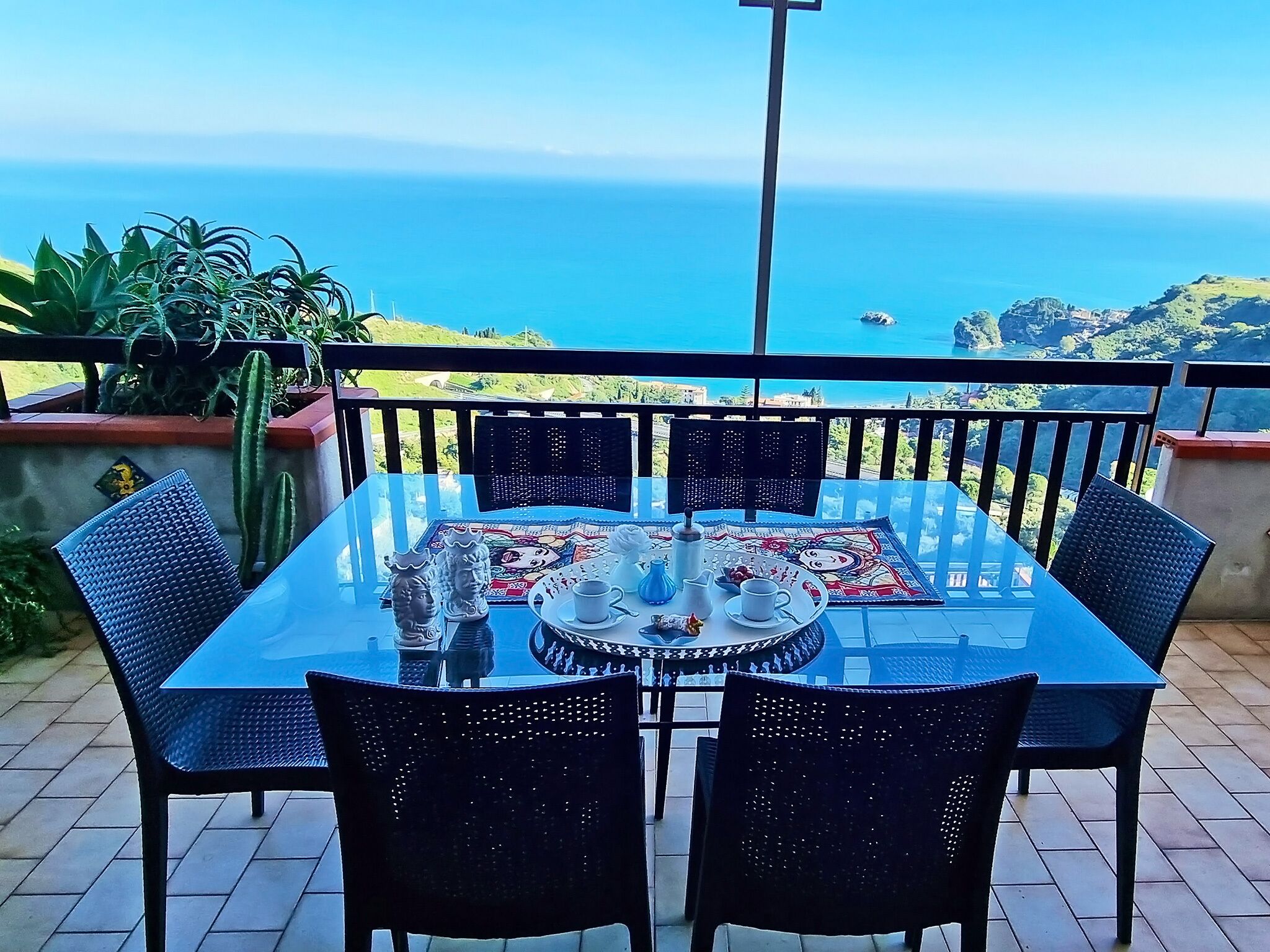 Une table avec un plateau en verre et des chaises, sur un balcon donnant sur la mer.