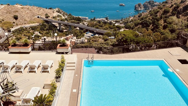 Una piscina al terrat amb gandules, vista al mar i un pont al fons.